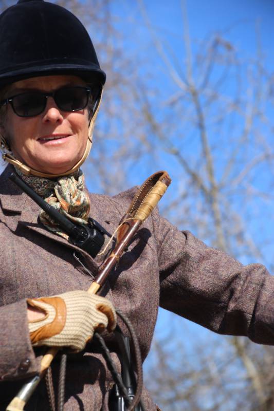 Woman in hunt attire smiling and holding whip