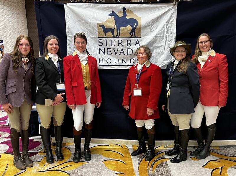 Six women in hunt attire standing in front of Sierra Nevada hounds banner