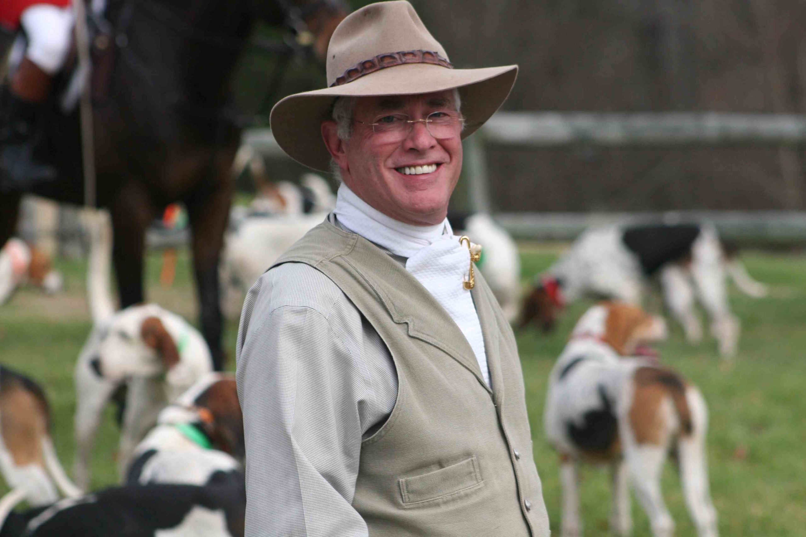 smiling man in vest with outback hat and hounds faded into background