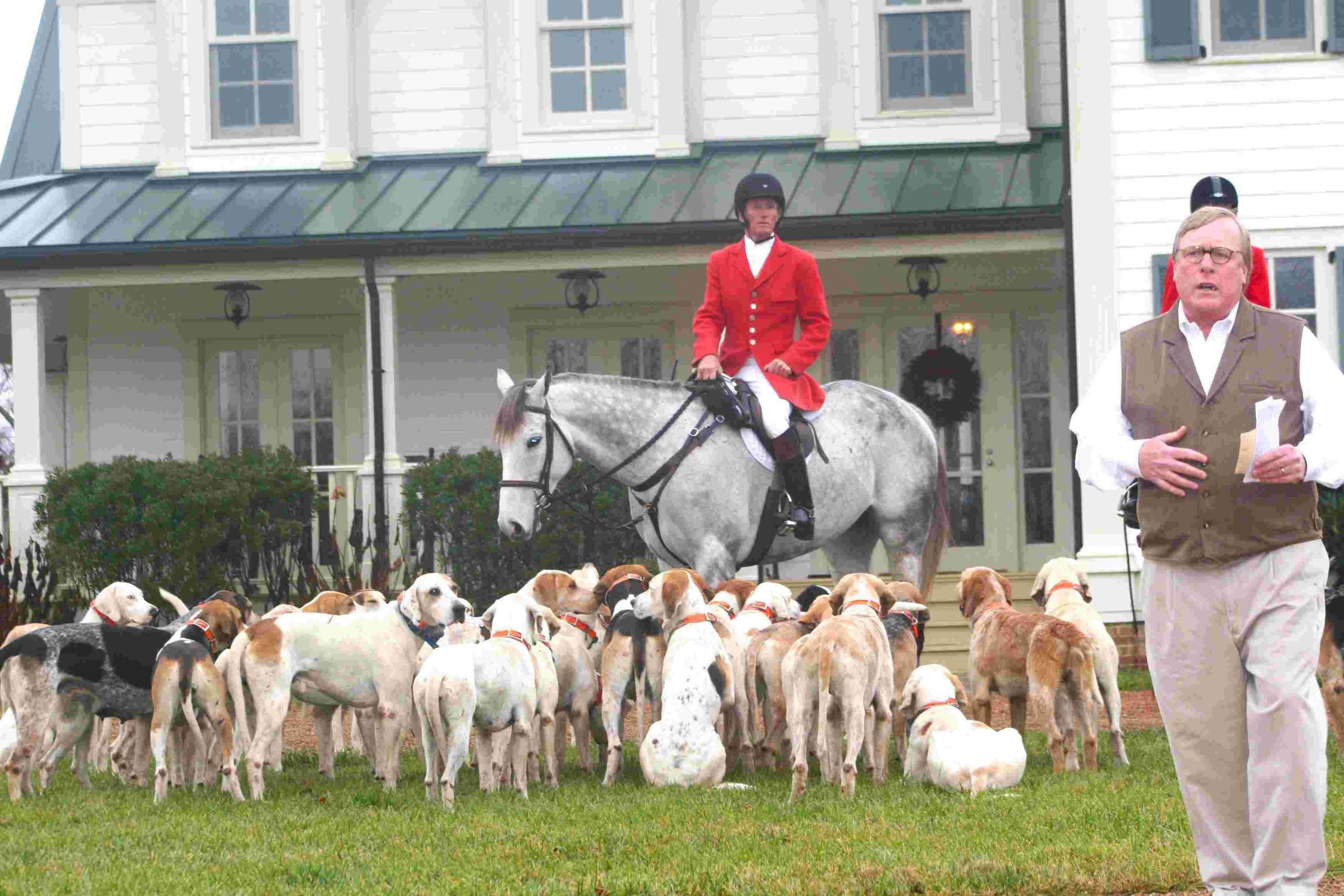 man walking away from huntsman and hounds in front of farm house