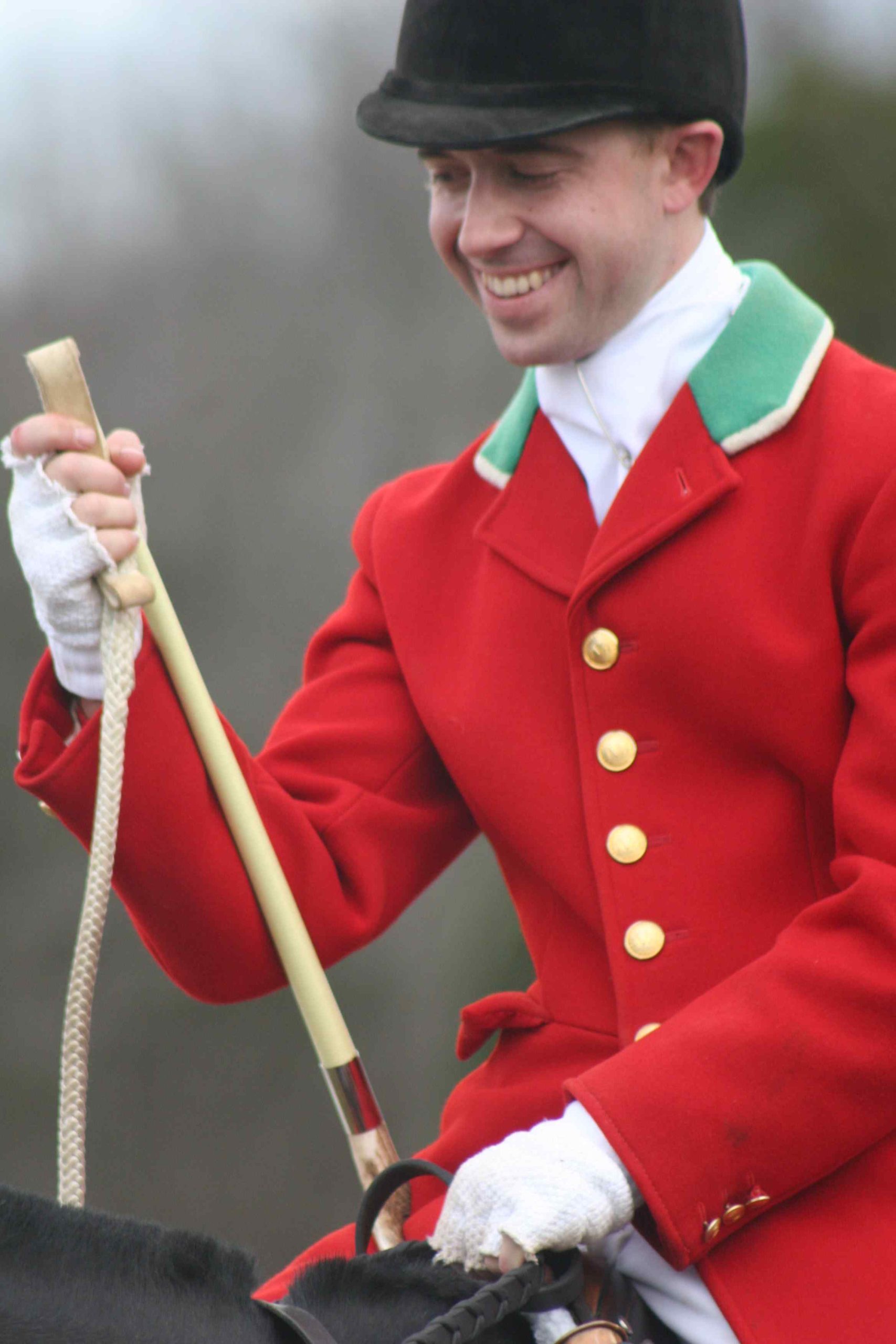 smiling huntsman with red coat and white hunt whip